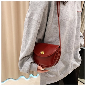Detail of dark red leather saddle bag featuring a gold rotary clasp and smooth finish