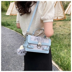 Vue d'un sac à bandoulière floral bleu clair et lilas avec un pompon en fourrure grise