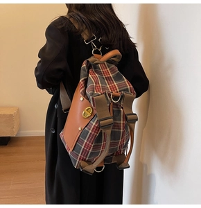 Close-up of vintage plaid canvas backpack featuring brown leather trim and golden oval twist lock