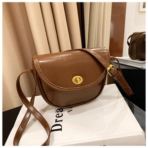 Close-up of vintage brown saddle bag with golden circular metal clasp and smooth PU leather