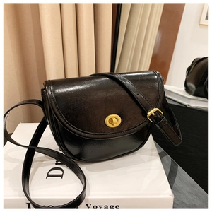 Close-up of a black leather saddle bag with a gold twist lock on a display stand