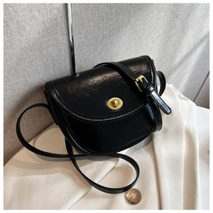 Detail of a vintage black saddle bag with a round gold metal lock and glossy finish