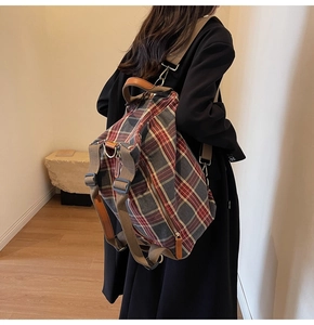 Detail view of a vintage plaid canvas backpack featuring brown leather trim and handles