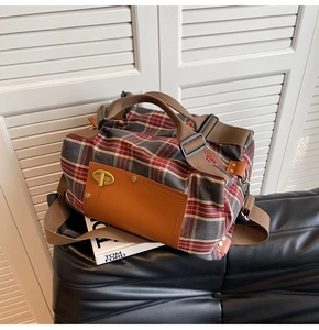 Detail of vintage red plaid canvas travel bag with leather accents on a black sofa