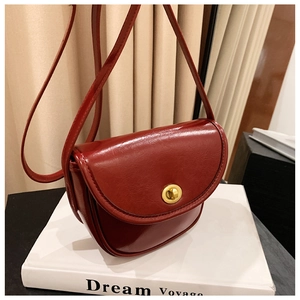 Detail of reddish-brown saddle bag featuring a vintage golden twist lock and leather texture
