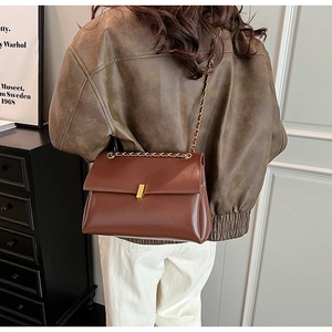 Sac cabas en cuir marron avec bandoulière chaîne dorée porté par un mannequin chic