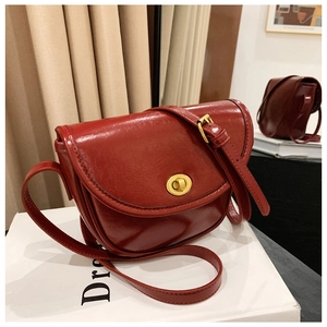 Detail of deep red retro saddle bag with gold twist lock and glossy embossed texture