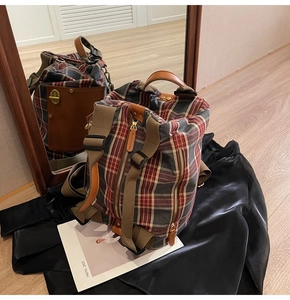Detail of British style red plaid canvas backpack featuring brown leather trim and side pocket