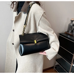 Détail d'un sac cabas noir avec fermoir doré et bandoulière chaîne porté à l'épaule