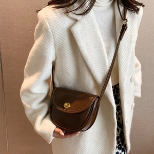 Classic dark brown leather saddle bag with gold swivel lock on a white wool coat