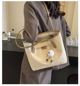Detailed side view of a large cream tote bag with brown leather trim worn by a model