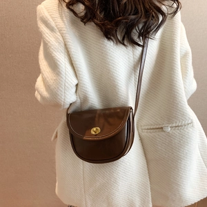 Minimalist dark brown saddle bag with gold buckle on model in white striped blazer
