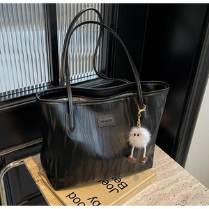 Detail of black tote bag with vertical wave texture and cute white pompom charm