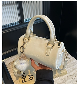 Détail du sac Boston crème avec breloque en peluche et ferrures dorées polies