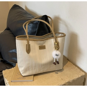 Detail of cream tote bag with wave texture, brown leather trim, and plush monster charm