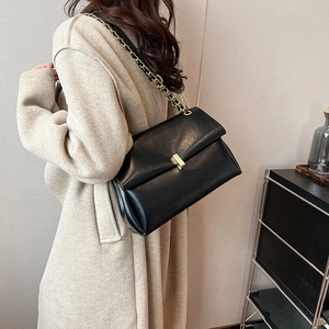 Sac fourre-tout noir en cuir avec chaîne dorée porté sur un manteau en laine beige
