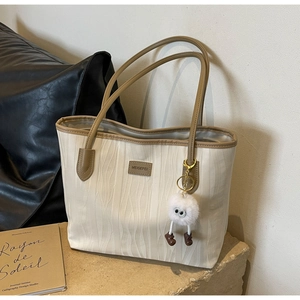Detail of white tote bag with wave texture, brown leather brand label and plush monster charm