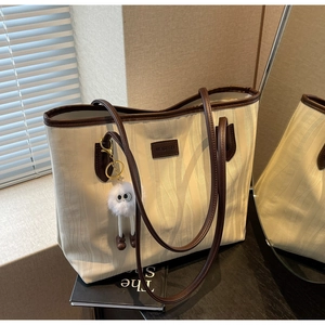 Detail of cream tote bag with vertical ripple texture, brown handles and plush charm