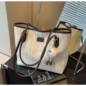 Detail of cream tote bag with wave texture, brown leather trim and plush pendant