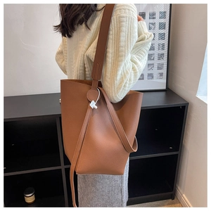 Detail view of brown textured leather bucket bag with wide shoulder strap on model