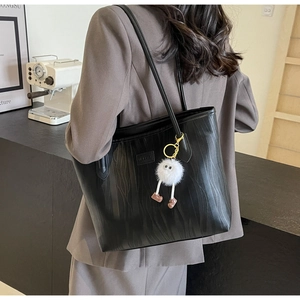 Detail of black textured tote bag featuring a white fuzzy charm and slender shoulder strap