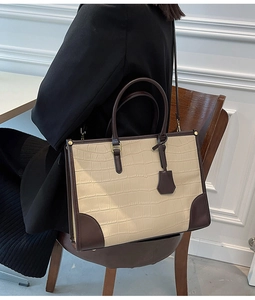 Detail of a white crocodile pattern tote bag with dark brown leather handles on a wooden chair