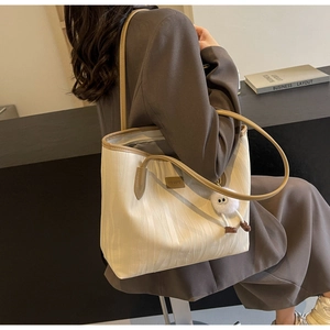 Detail view of large cream tote bag featuring vertical wavy texture and brown leather trim