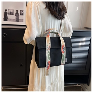 Detail der schwarzen Canvas-Tasche mit floralem Webband an einem Modell im weißen Kleid