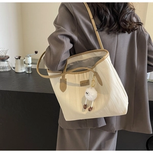 Detail of cream tote bag with wave texture, brown leather trim and plush pendant charm