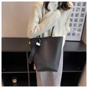 Detail of black large bucket bag featuring pebbled leather texture and wide shoulder strap