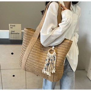 Détail d'un sac cabas en paille tressée avec breloques œil bleu et pompons blancs