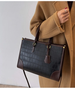Close-up of black crocodile pattern tote bag with brown leather trim and gold hardware