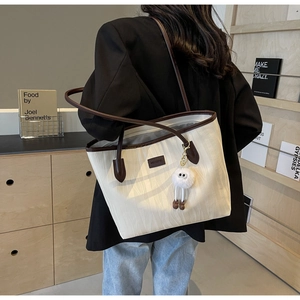 Detail of cream tote bag with wave texture, brown leather handles and plush charm