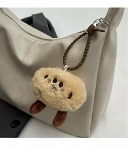Detail van een pluizige aardappelmonsterhanger aan een crèmekleurige draagtas met riem