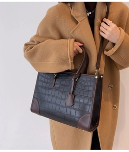 Detail of black crocodile texture tote with brown leather trim and gold metal hardware