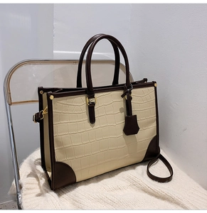 Detail of faux crocodile texture and gold hardware on two-tone cream tote bag