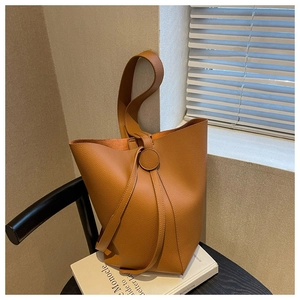 Detail of tan lychee grain leather bucket bag featuring a round buckle and shoulder strap