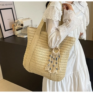 Détail du sac cabas en paille beige avec pompon bohème et perles d'œil bleu porte-bonheur