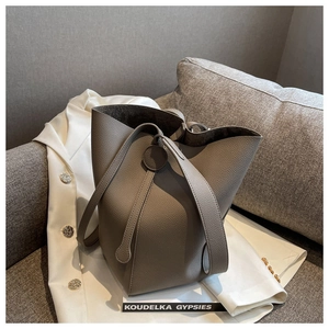 Detail of grey lychee leather bucket bag with top handle on a neutral lifestyle background