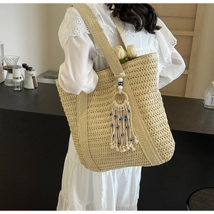 Détail du sac cabas en paille tissé à la main avec breloque œil bleu et bandoulière tressée