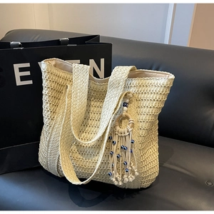 Détail du sac cabas en paille avec pompons bohèmes et perles de l'œil du mal bleues