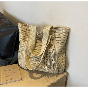 Détail du sac cabas en paille beige avec pompon bohème et perles décoratives mauvais œil