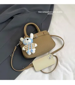 Detailed top view of a khaki pebble leather bucket bag with a plush rabbit charm and phone