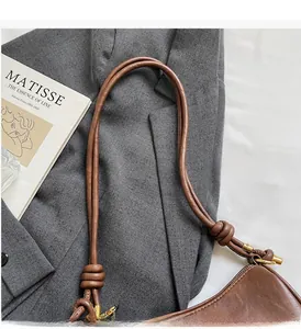 Detail view of a brown leather shoulder bag featuring a knotted strap on a gray suit