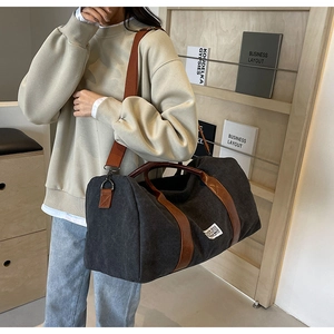 Grand sac de voyage en toile noire avec poignées en cuir marron et bandoulière réglable