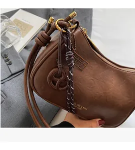 Detail of dark brown leather half-moon shoulder bag featuring a side knot and brand logo