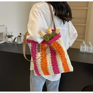 Detail einer großen Stroh-Einkaufstasche mit rosa-orangen Streifen und Lederriemen