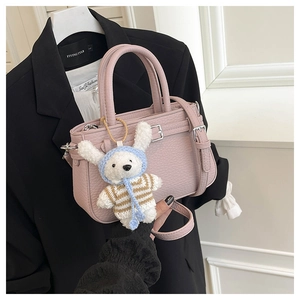 Detail of pink lychee grain PU leather handbag with a cute plush bunny charm and shoulder strap