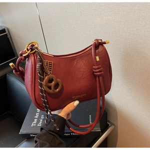 Detailed close-up of dark wine red leather shoulder bag with knotted handle and gold logo