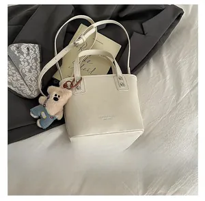 Détail du sac seau beige avec logo de marque et accessoire d'ours en peluche mignon